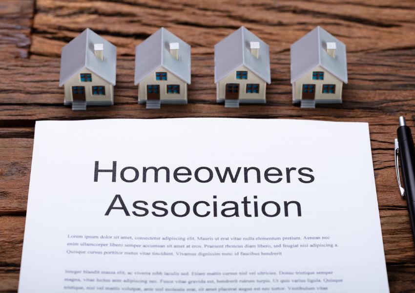 Four miniature houses sit on a wood desk above a document titled 'Homeowners Association'.