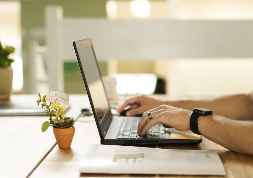 A property manager completes administrative tasks on a black laptop at a desk; a plant sits next to the laptop.