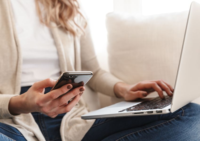 A landlord holds their phone while typing on their laptop, responding to tenant requests.