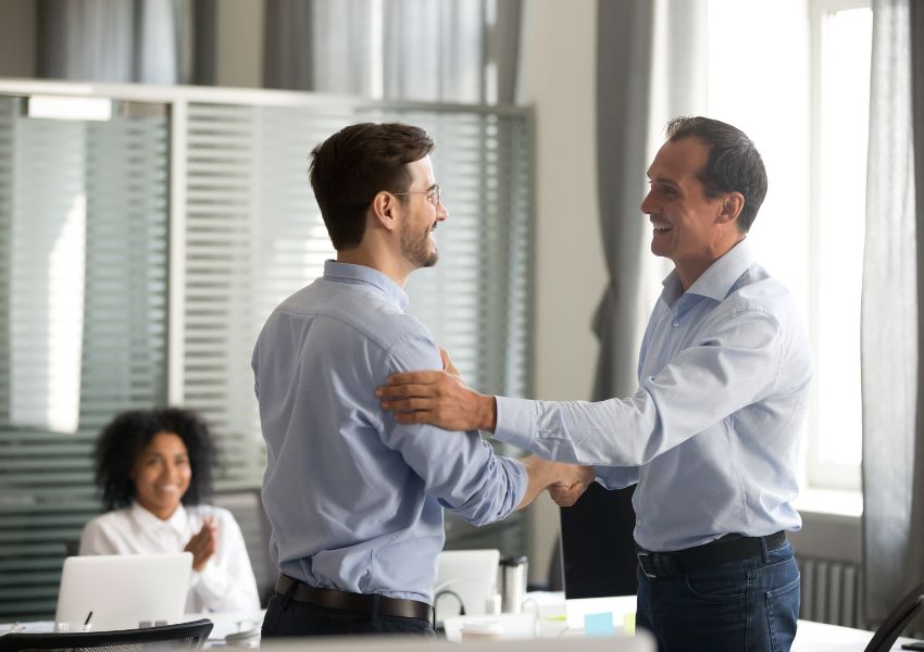 A landlord shakes hands with a tenant in an office, both in button down shirts.