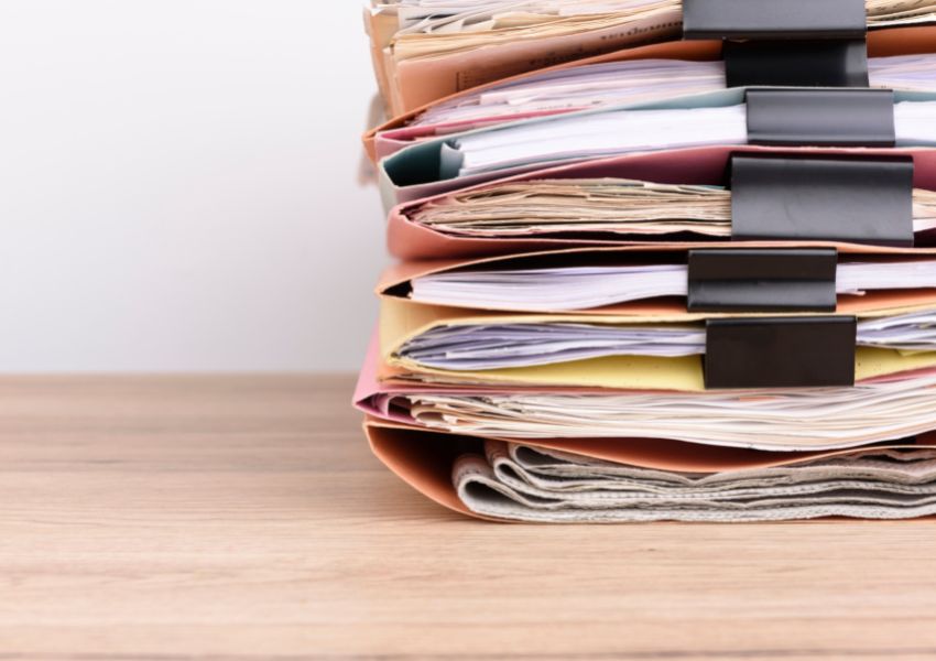 A landlord's pile of financial records and documents sits to the right on a wood desk, organized meticulously by property and contained in folders.
