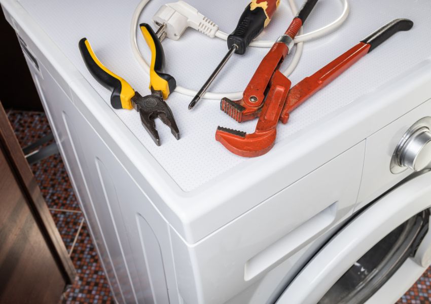 A laundry machine is pictured with a wrench, screwdriver and another maintenance tool on its surface.