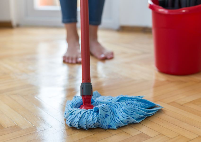 Light hardwood floors are being cleaned by a barefoot tenant with a blue and red mop.
