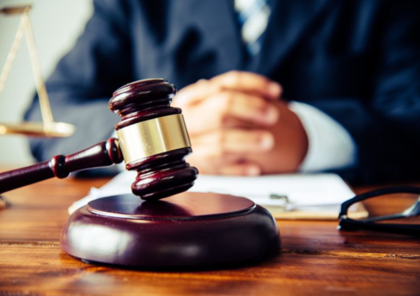 A dark brown gavel is pictured in front of a judge’s hands, resting on their desk.