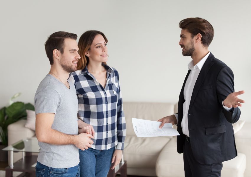 A landlord in a suit speaks with two prospective tenants about the rental property.
